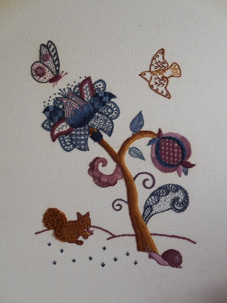 Tree of Life in Crewelwork, with a squirrel on the ground, a bird and a butterfly in the sky and a fantasy flower and pomegranate on a tree trunk, in shades of blue and brown